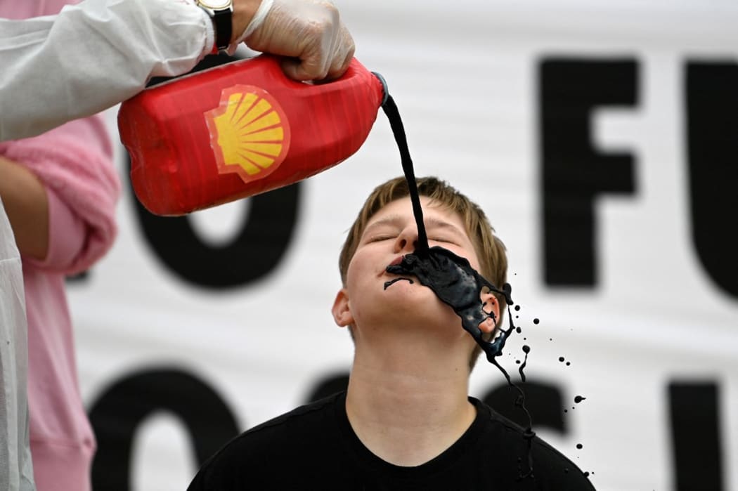 Activists from the climate change protest group Extinction Rebellion,  pour a black liquid to represent oil, into the mouth of a fellow activist as they demonstrate against oil giant Shell on the beach in St Ives, Cornwall on June 11, 2021, on the first day of the three-day G7 summit.