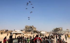 People gather as a C-130 Hercules military transport aircraft drops humanitarian aid on the northern Gaza Strip on 27 July, 2025.