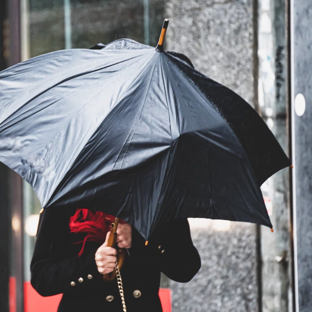 A woman has difficulty holding an umbrella from strong winds in rainy weather.