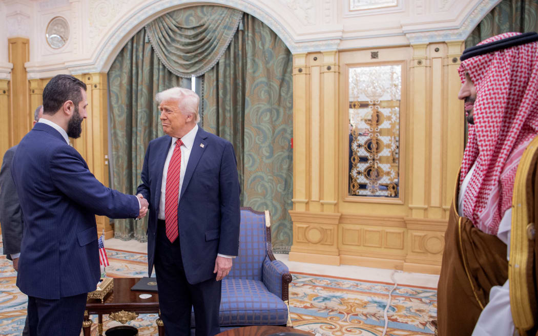 A handout picture provided by the Saudi Royal Palace shows Saudi Crown Prince Mohammed bin Salman (R) watching as US President Donald Trump (C) shakes hands with Syria's interim president Ahmed al-Sharaa in Riyadh on 14 May, 2025.