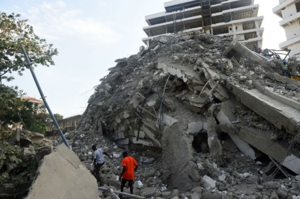 People walk to rescue workers from the rubble of a 21-storey building under construction that collapsed at Ikoyi district of Lagos, Nigeria