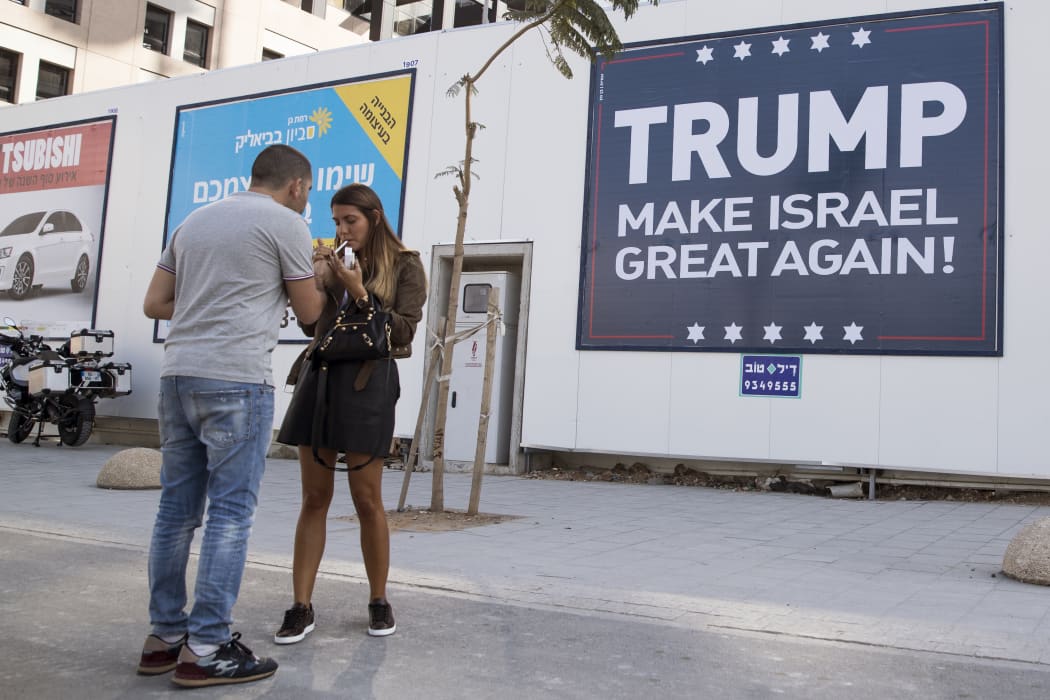 Two people stand in front of a 'Trump make Israel great again!' sign in Israel