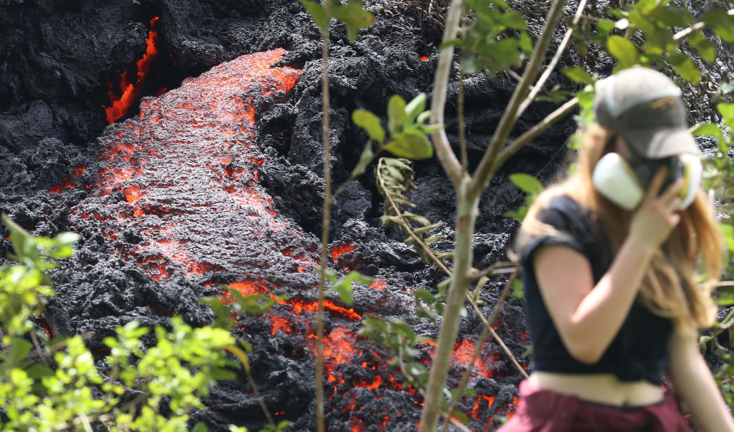 Lava flows at a new fissure in the aftermath of eruptions from the Kilauea volcano on Hawaii's Big Island as a local resident walks nearby after taking photos.