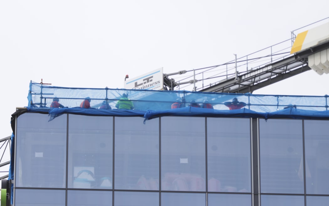Construction workers can be seen at the top of a building at the centre of a serious shooting incident in downtown Auckland on 20 July, 2023.