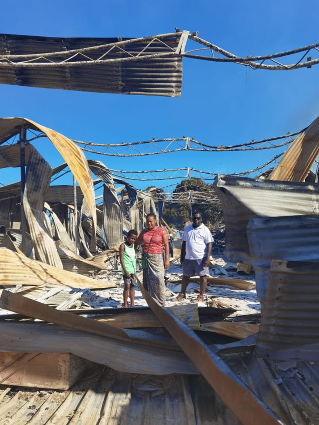 Namoi Kaluae with her husband and son amid what's left of their 10-year-old business.