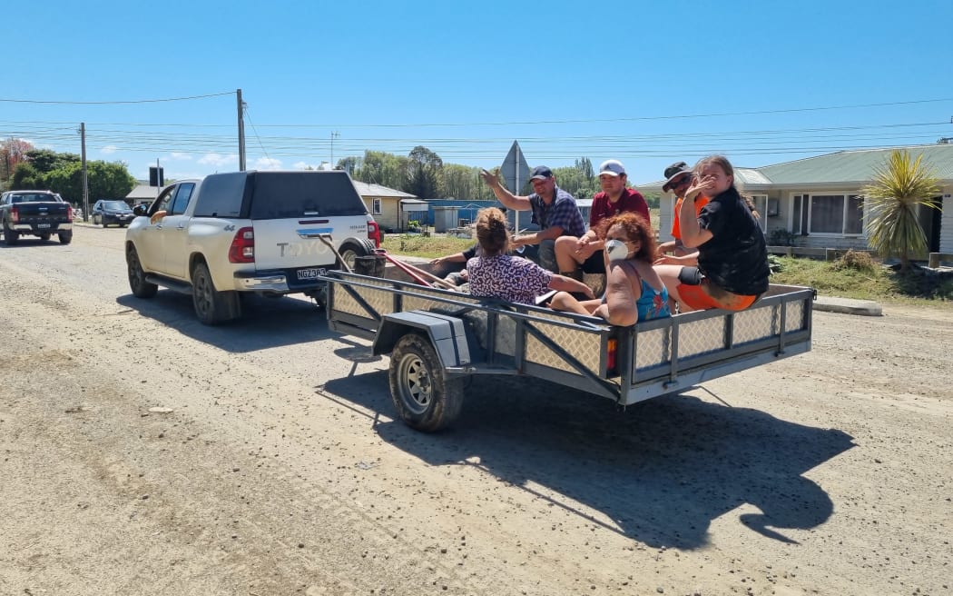 People ride on the back of a trailer pulled along by a ute.