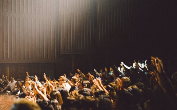An audience in an auditorium, voting with raised hands.
