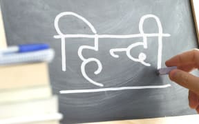 Hand writing on a blackboard in a Hindi class. Some books and school materials. Indian language