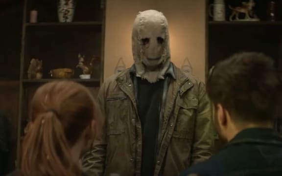 A man in a spooky mask faces a young white heterosexual couple