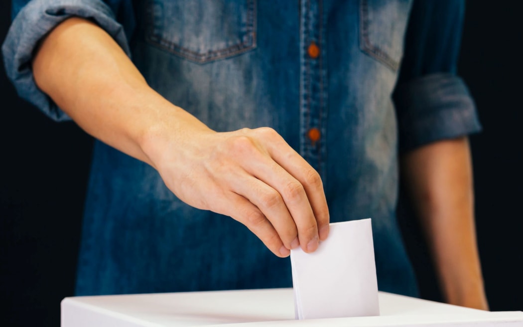 Front view of person holding ballot paper casting vote at a polling station for election vote in black background