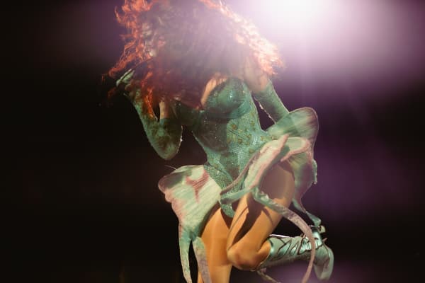 Chappell Roan, wearing a tight green cartoonish dress, jumps in the air as her hair falls in her face.