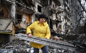 A woman clears debris at a damaged residential building at Koshytsa Street, a suburb of the Ukrainian capital Kyiv, where a military shell allegedly hit, on February 25, 2022.