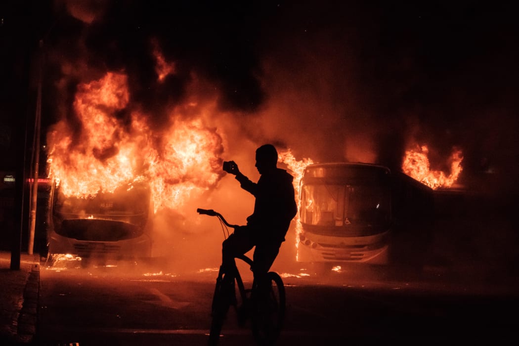 A man on a bicycle takes pictures of buses that were set on fire by protesters during the nationwide strike called by unions opposing austerity reforms in Rio de Janeiro, Brazil, on April 28, 2017.