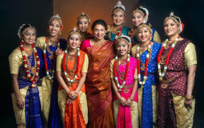 A group of young women in traditional Indian garb surround their dance teacher a middle age Indian woman.