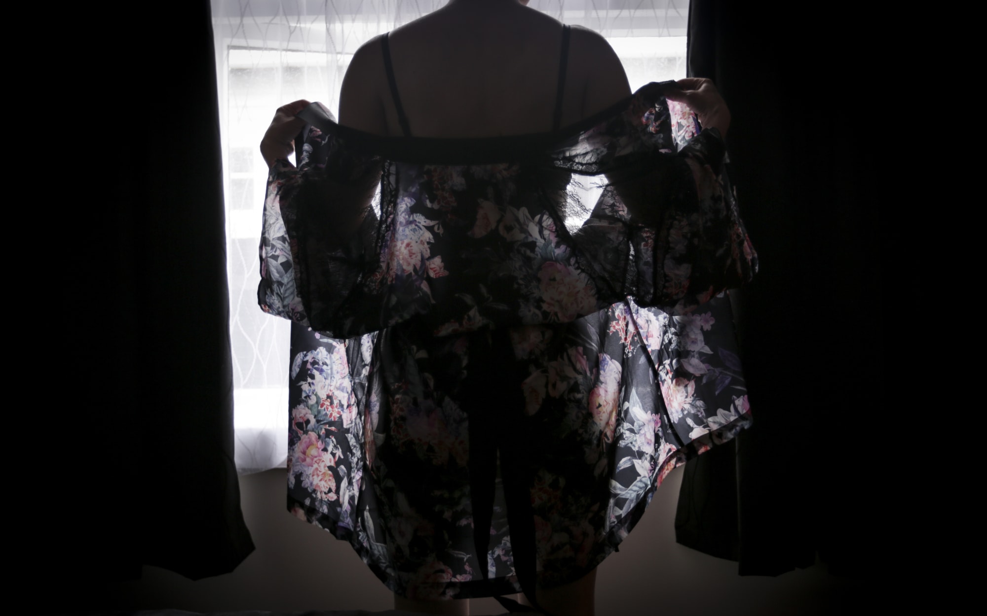 Woman stands silhouetted against window in lingeries and drapy wrap