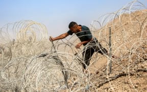 A man attempts to remove parts of the barbed-wire fence at the so-called "Netzarim corridor" near Nuseirat in the central Gaza Strip on October 10, 2025, as people make their way back to Gaza City. Gaza's civil defence agency said on October 10 that Israeli forces have begun pulling back from parts of the territory, particularly in Gaza City and Khan Yunis. Israeli prime minister's office said that the government had "approved the framework" of a hostage release deal with Hamas, as both sides edged closer to ending more than two years of hostilities in Gaza. (Photo by Eyad BABA / AFP)