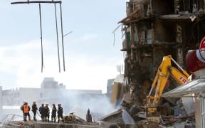Rescuers stand at the smoking ruins of the CTV building, where 115 people died, in Christchurch on 24 February, 2011, two days after the deadly earthquake.