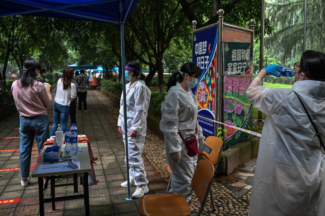 Workers stand next to Wuhan residents wearing face masks waiting in a line to be tested of COVID-19 in a neighborhood in Wuhan, in China's central Hubei province on May 15, 2020.