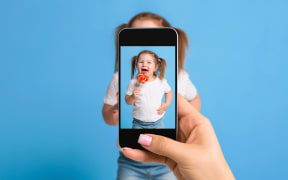 Woman's hand making photo of a little girl with a mobile phone. Selective focus on a mobile phone with a portrait of a girl. Made for social networks