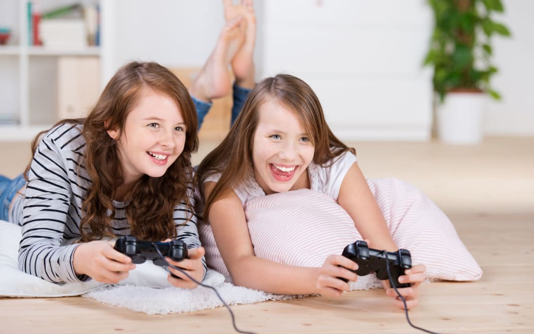 A photo of two young girls happily playing video games in a console laying on the living-room floor