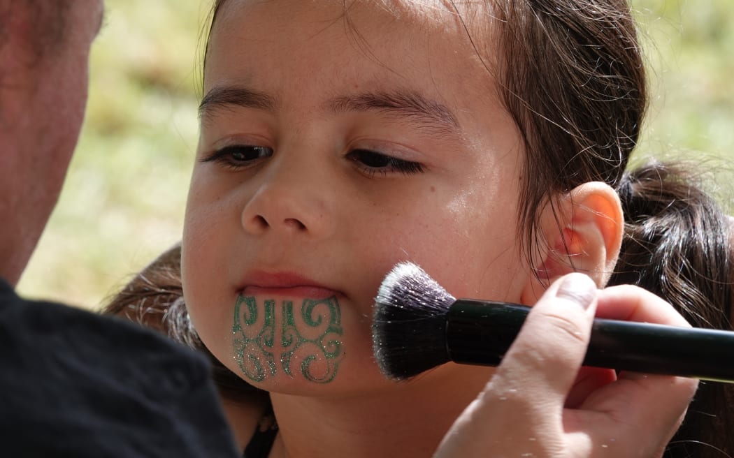 A young festival-goer has glitter applied to her stencilled moko kauae.