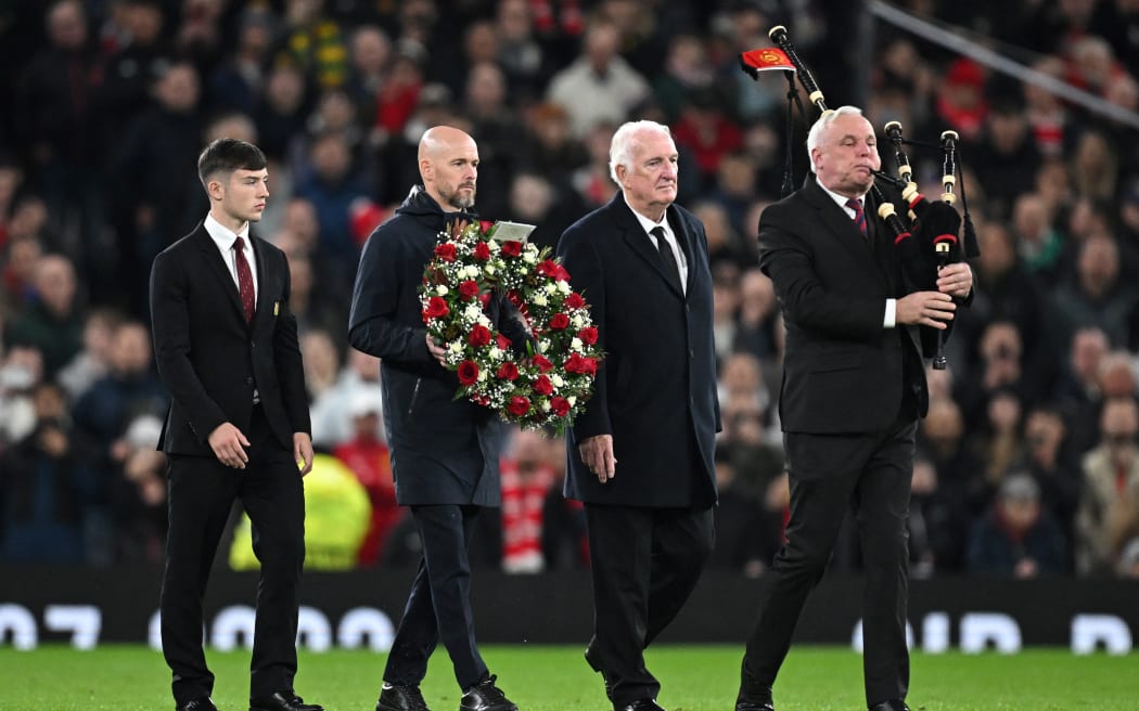 Manchester United's Dutch manager Erik ten Hag carries a wreath of flowers next to former Manchester United's player Alex Stepney and Manchester United youth player Dan Grove as they are accompanied by a pipe player during a tribute to late Manchester United player Sir Bobby Charlton.