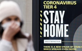 A pedestrian wearing a mask walks past a sign alerting people that Covid-19 cases are very high in London on December 23, 2020.