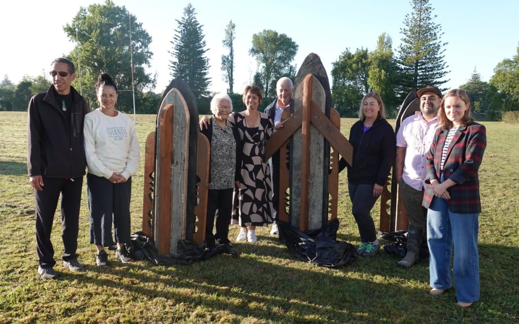 Council staff and dignitaries stand next to three pou on the grass.