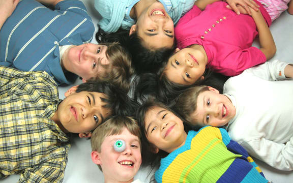 A photo of seven mixed race children all lying with their heads in a circle