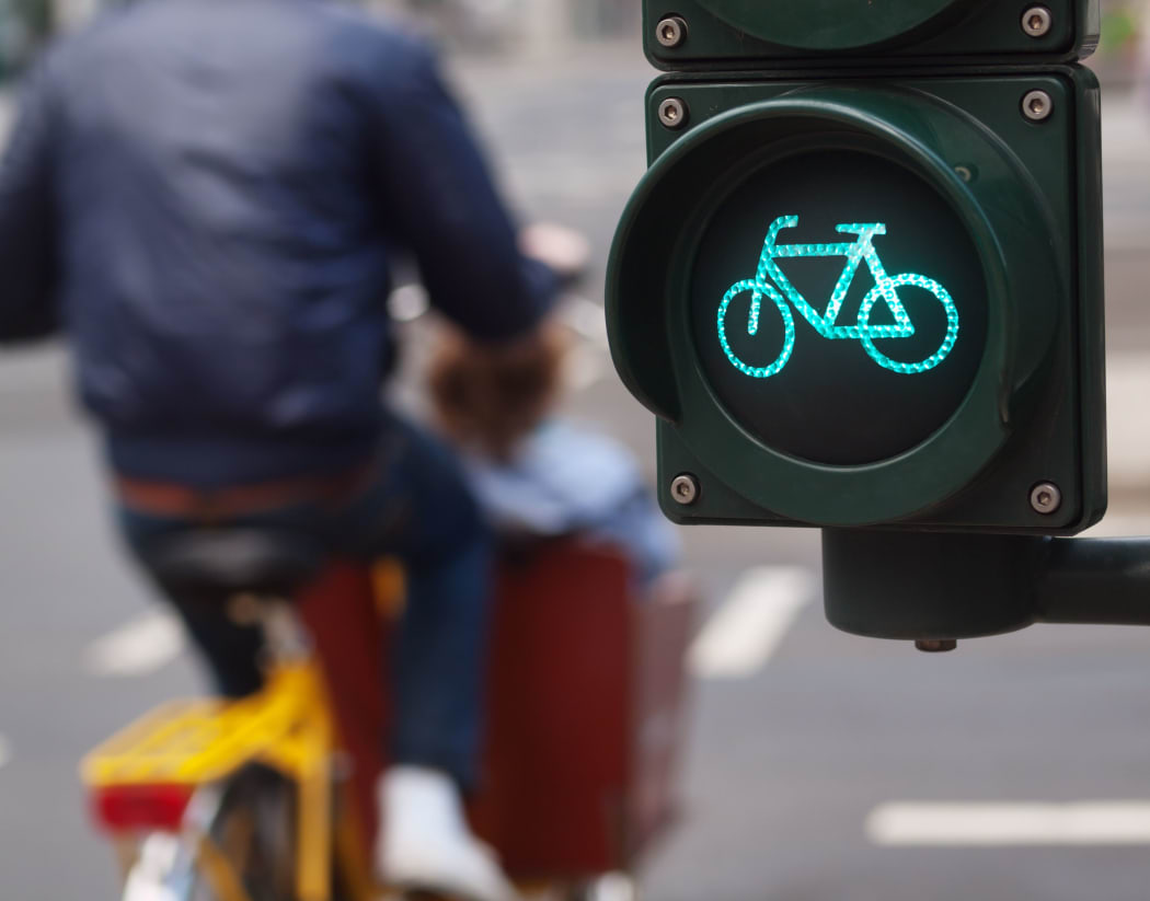 A cyclist passes a green cycling traffic light in a city.