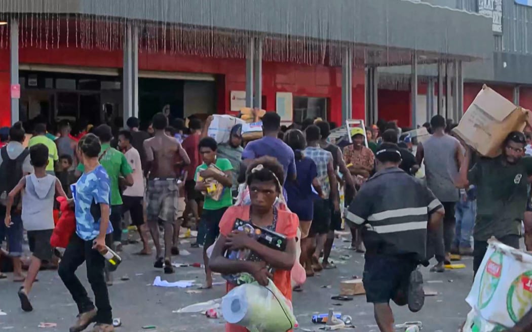 This screen grab from AFPTV video footage taken on January 10, 2024 shows people carrying items as crowds leave shops with looted goods amid a state of unrest in Port Moresby. A festering pay dispute involving Papua New Guinea's security forces on January 10 sparked angry protests in the capital, where a crowd torched a police car outside the prime minister's office. By Wednesday afternoon pockets of unrest had spread through the capital Port Moresby, with video clips on social media showing crowds looting shops and stretched police scrambling to restore order.