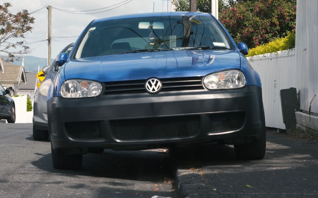 Pedestrians try to use the footpath in Auckland where cars are parking over the kerb.