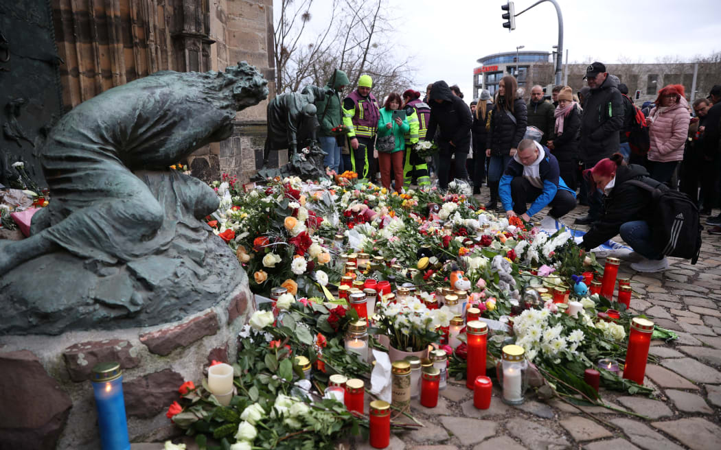 People lay flowers and candles at the site of a car-ramming attack on a Christmas market in Magdeburg, eastern Germany, on December 21, 2024, resulting in several deaths and dozens of injured. - German media reports that the death toll has risen to four over night and up to 200 injured in the attack on December 20th. (Photo by Ronny HARTMANN / AFP)