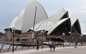 A few people walk along Circular Quay outside the Opera House in Sydney on March 25, 2020, as people stay away due to restrictions to stop the spread of the worldwide COVID-19 coronavirus outbreak.