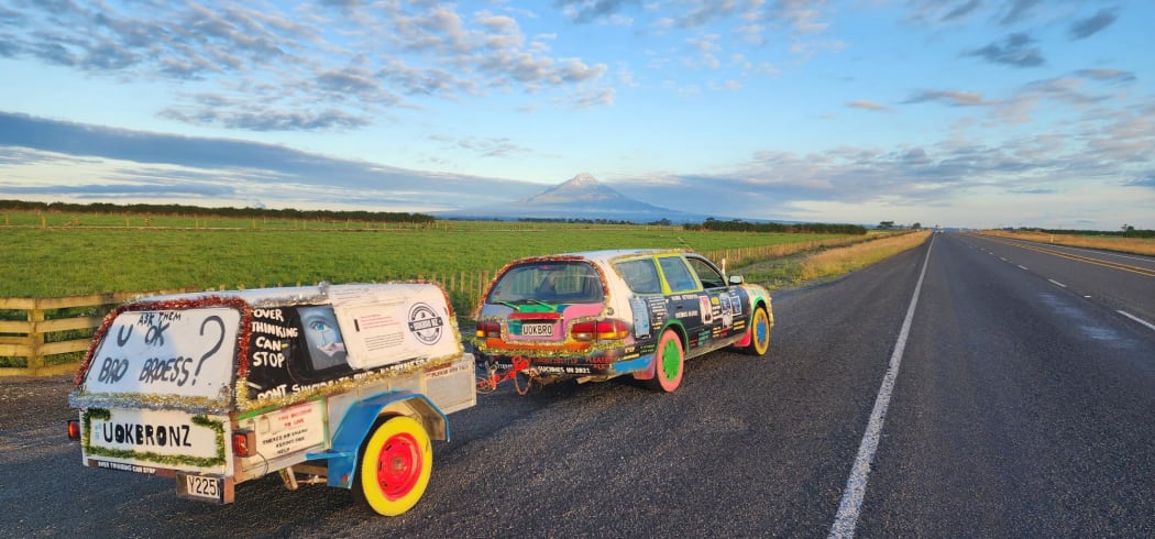 A colourfully decorated car pulled up on a roadside with Mount Taranaki in the background.