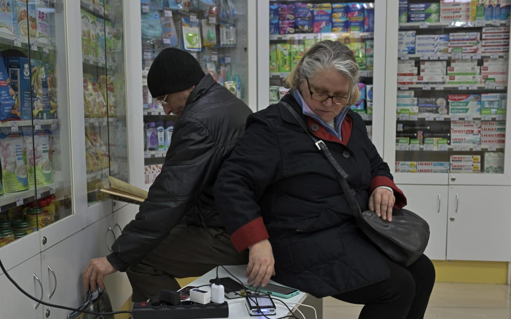 People charge their devices in a pharmacy powered by a generator, during blackout in Kharkiv, on March 22, 2024, amid the Russian invasion of Ukraine. In Kharkiv, Ukraine's second-largest city with a pre-war population of nearly one and a half million, street lighting is switched off, no lights appear in the windows of buildings, and the pavement is only occasionally illuminated by car headlights following massive night-time strikes on March 22, 2024.