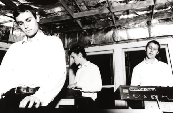 Bressa Creeting Cake are three young in white shirts looking down while playing instruments.