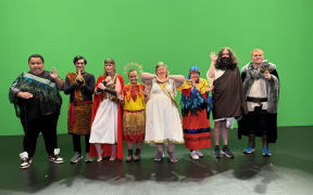 A group of performers pose in costume in front of a green screen.