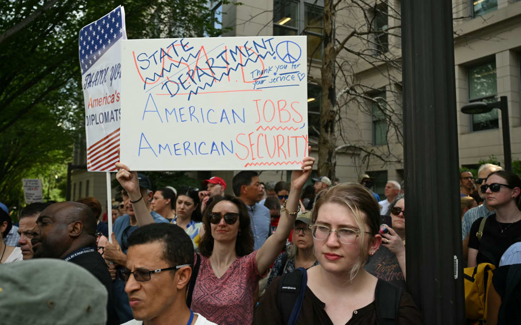 Supporters of fired US State Department workers hold signs outside the building in Washington, DC, on July 11, 2025. The US State Department began laying off more than 1,300 employees as part of President Donald Trump's campaign to massively downsize the federal government workforce. A State Department official said 1,107 members of the civil service and 246 Foreign Service employees were being informed that they were being fired. (Photo by SAUL LOEB / AFP)