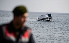 A sinking boat is seen behind a Turkish gendarme off the coast of Turkey.