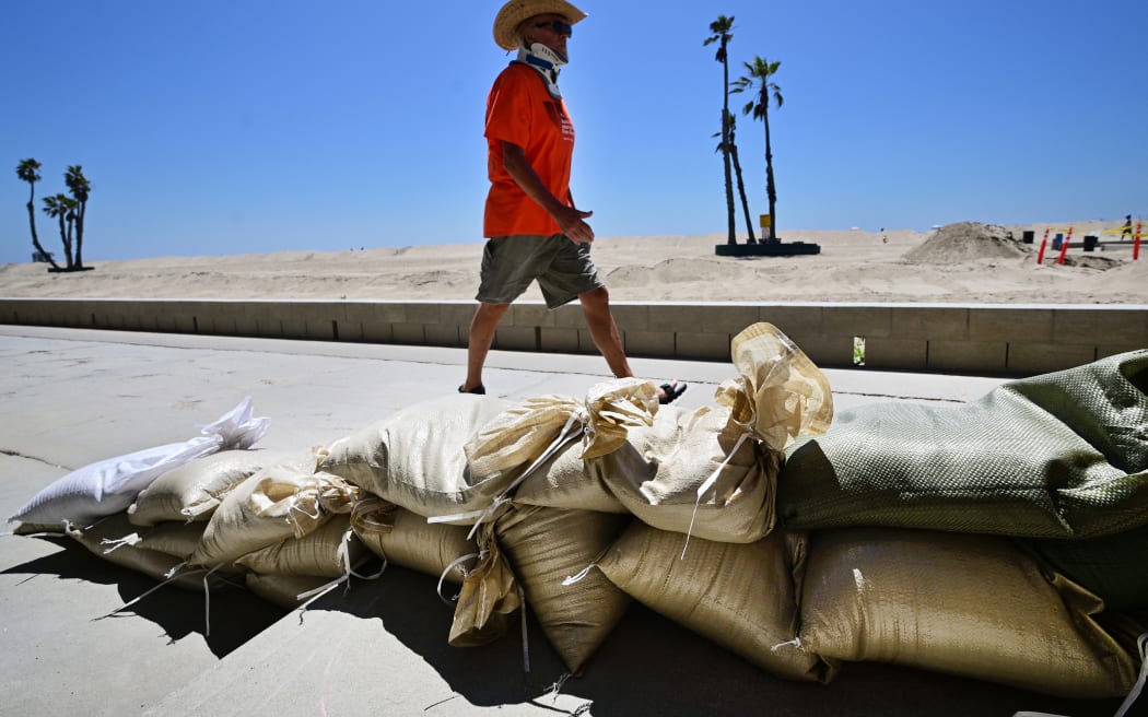 A man walks past sand bags placed to protect beach front homes in Seal Beach, California on August 18, 2023, as they prepare for hurricane Hilary. Hilary strengthened into a Category 4 hurricane on August 18, 2023 and was expected to further intensify before approaching Mexico's Baja California peninsula over the weekend, the US National Hurricane Center (NHC) said. In the US, parts of southern California and southern Nevada could see heavy rain through early next week, the NHC said. (Photo by Frederic J. BROWN / AFP)