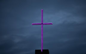 A neon cross lit up against a moody early morning sky