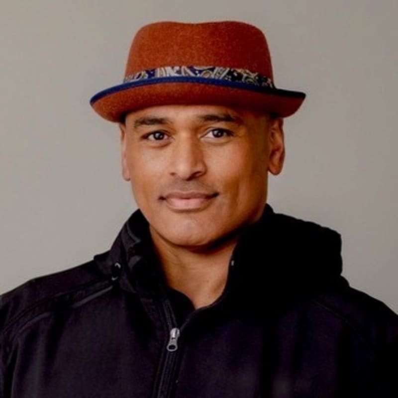 Image of Murdoch Ngahau smiling softly at camera. He wears a small brown rimmed hat and black jacket.