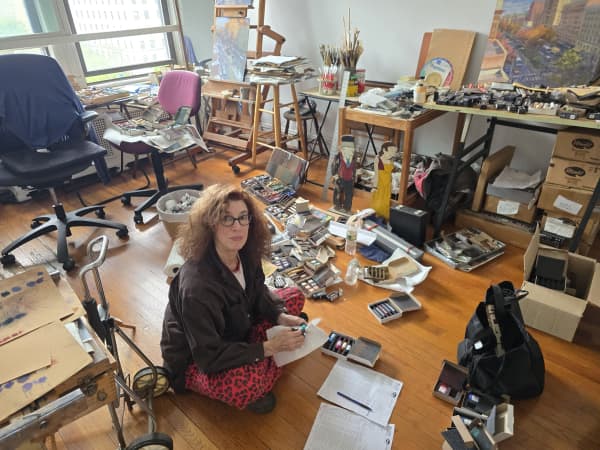 Artist Jane Rosenberg sits on the floor of her Manhattan studio, cleaning her pastels, surrounded by trays and boxes of art supplies and paintings.