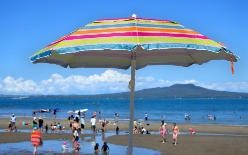 Colourful beach umbrella on a summer sunny day above unrecognizable people on a beach at the north shore of Auckland, New Zealand