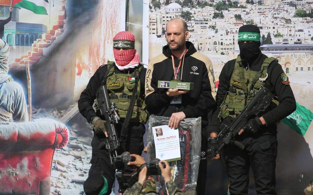 Israeli-Argentinian hostage Yair Horn (C) stands next to Palestinian militants as others take pictures of him on stage during a handover to a Red Cross team in Khan Yunis in the southern Gaza Strip on February 15, 2025, as part of the sixth hostage-prisoner exchange. Masked Hamas and Islamic Jihad militants handed over three Israeli hostages to the Red Cross in Gaza on February 15, in the sixth hostage-prisoner swap under a ceasefire agreement with Israel, an AFP journalist reported. (Photo by Eyad BABA / AFP)