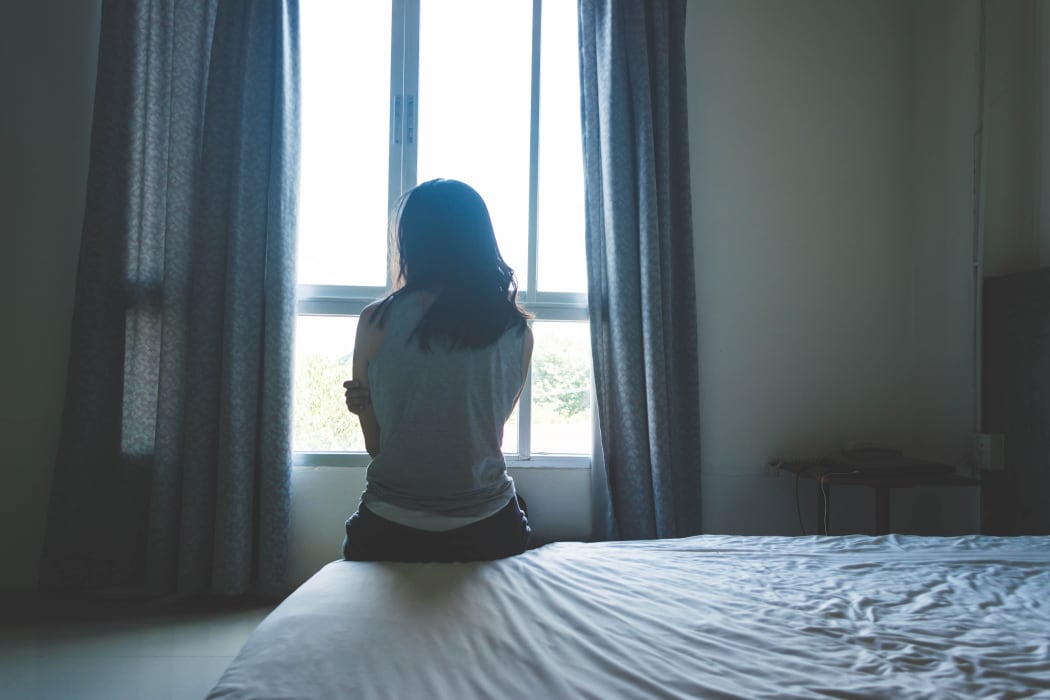 woman sitting on bed in room with light from window (abuse concept)