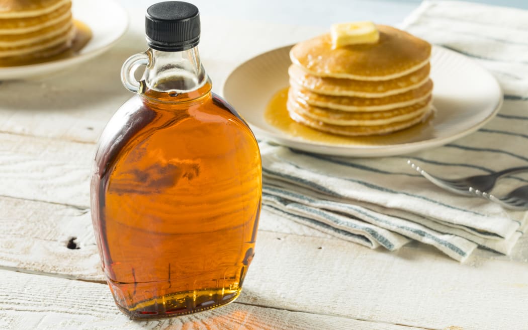 Maple syrup with some pancakes in the background.