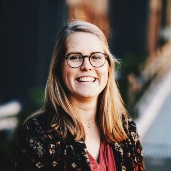 A headshot of a woman with long blonde hair and glasses. She is smiling at the camera.