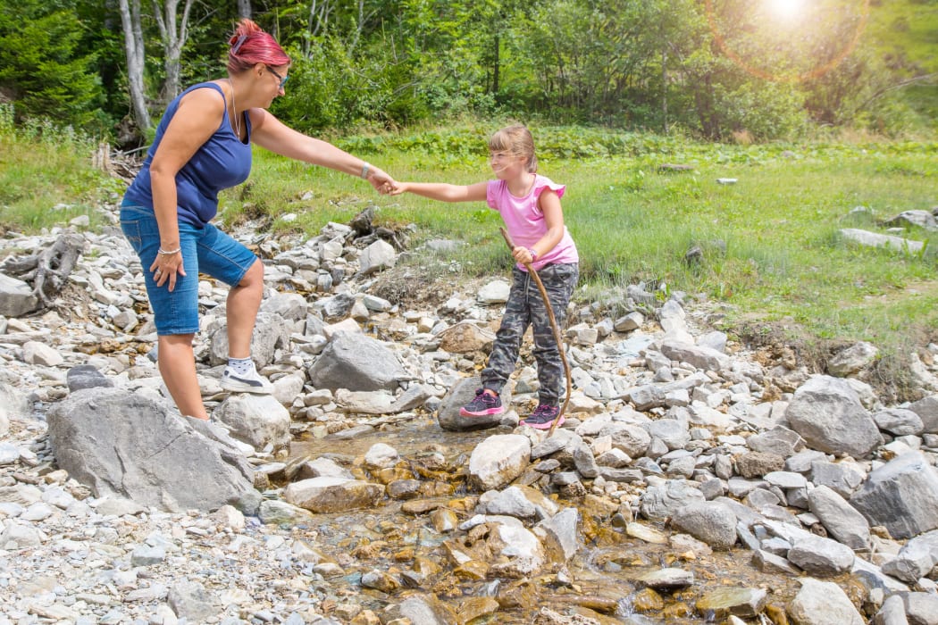 A photo of a mother helping her daughter across a stream